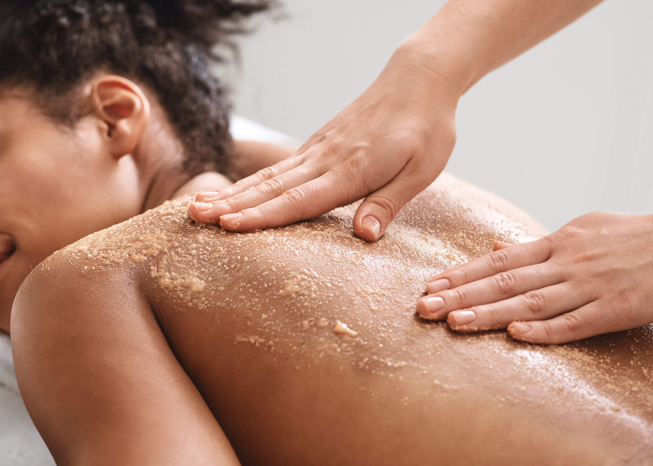 Frau erhält eine Peeling-Massage für den Rücken, Nahaufnahme der Hände, die das Peeling auf ihre Haut auftragen. - Hotel La Casies Mountain Living