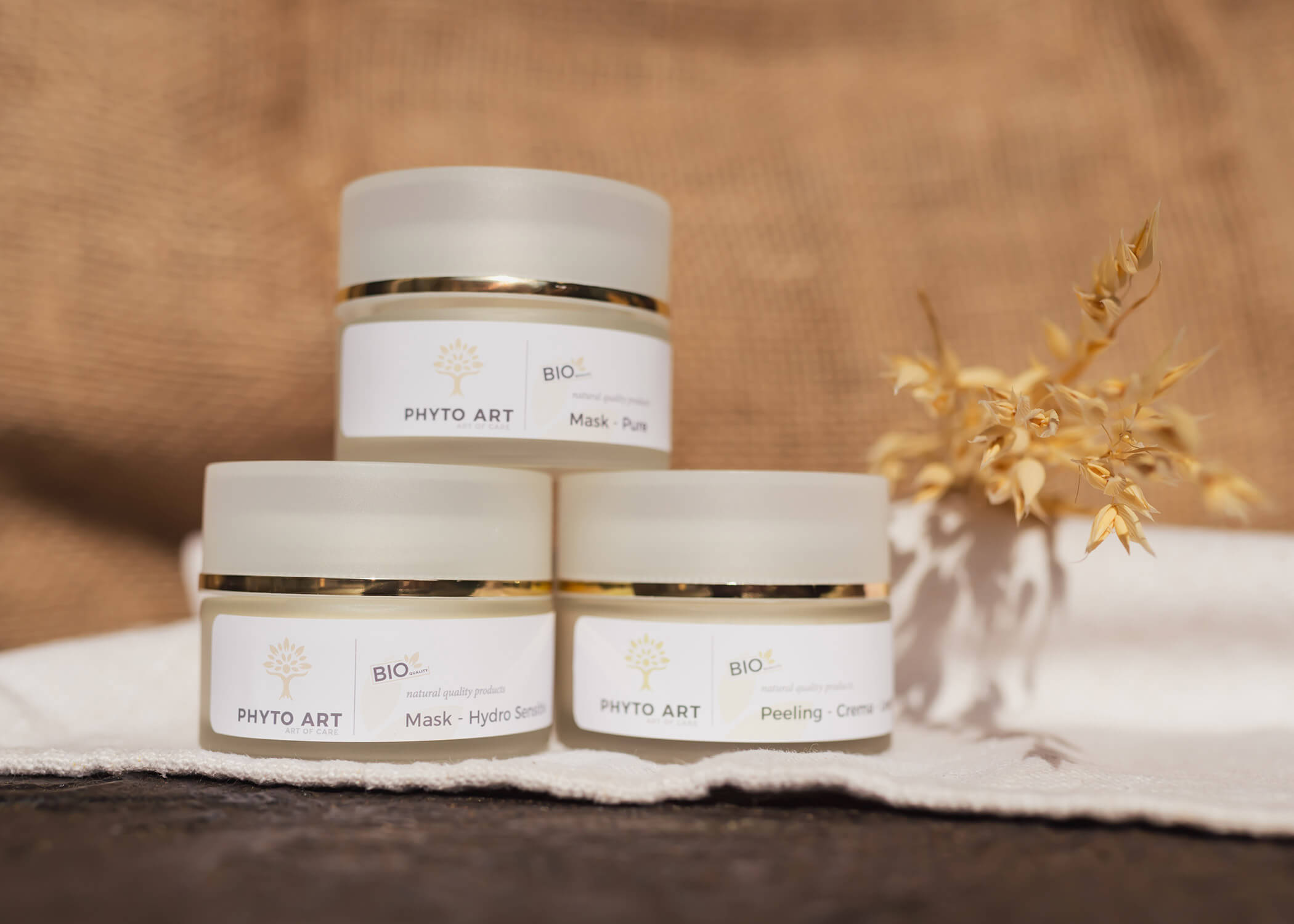 Drei PHYO ART Hautpflegetiegel auf einem weißen Tuch gestapelt, daneben getrocknete Blumen. - Hotel La Casies Mountain Living