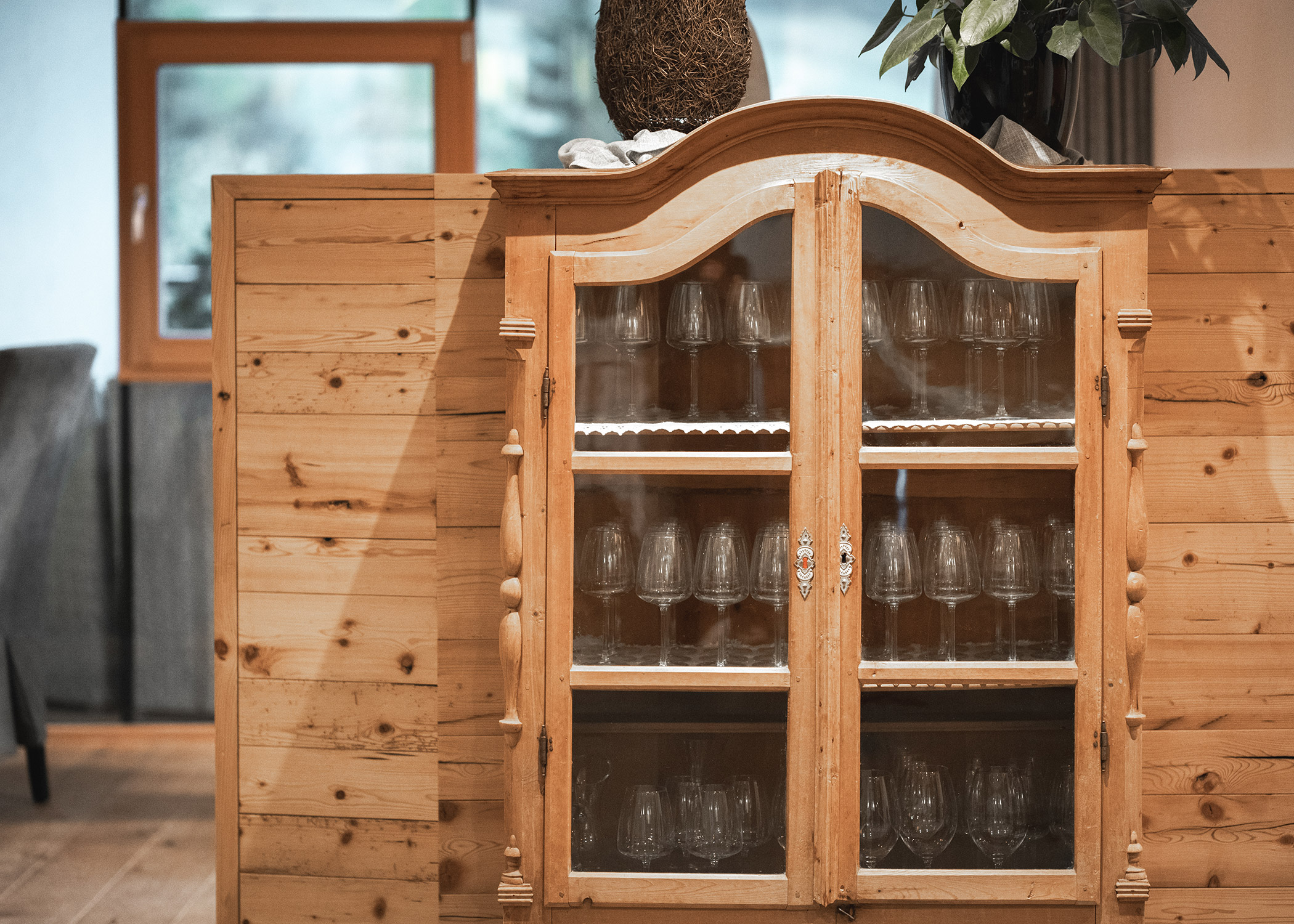 In einem Holzschrank mit Glastüren stehen mehrere Reihen von Trinkgläsern. - Hotel La Casies Mountain Living