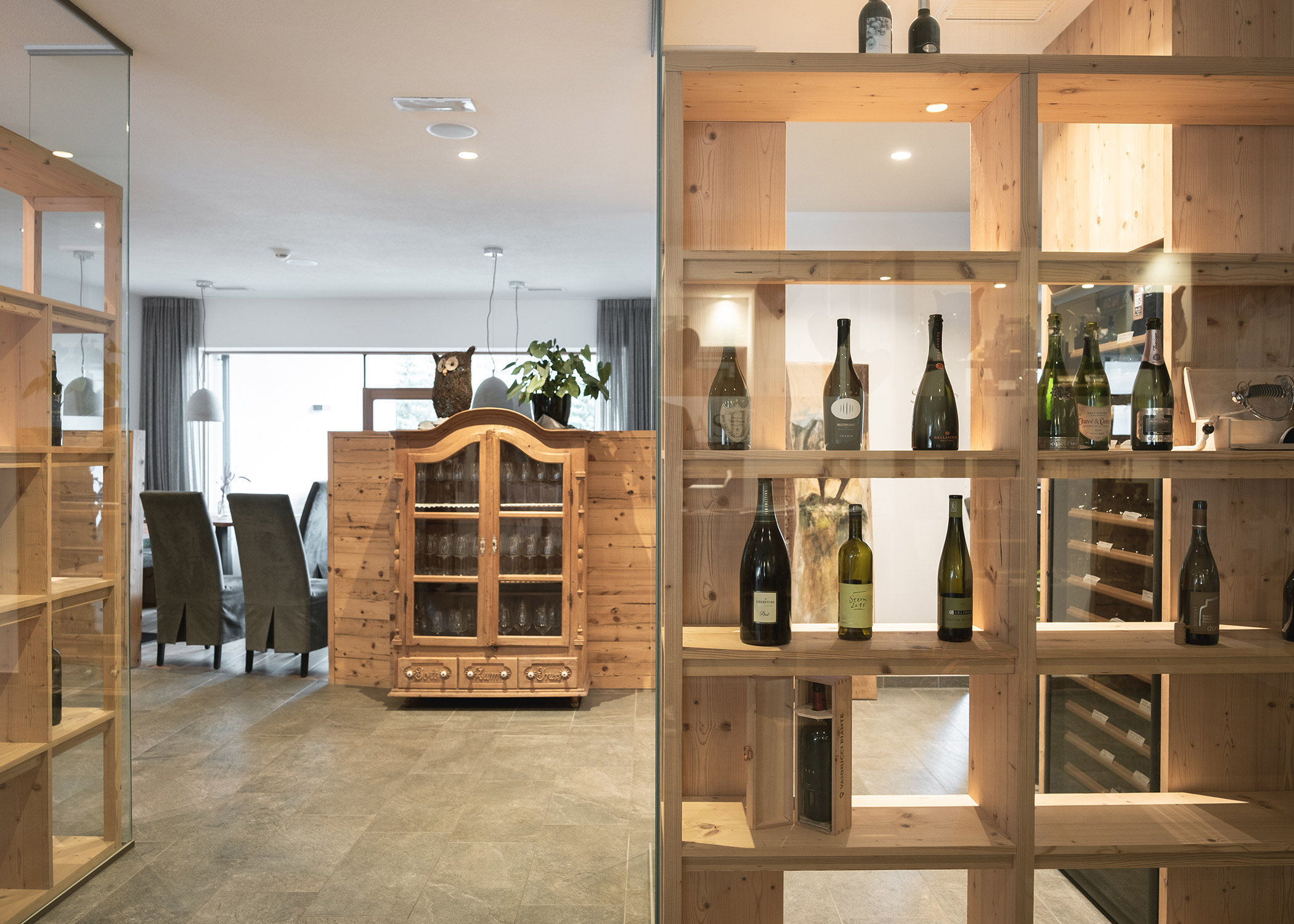 Holzregale mit Weinflaschen in einem modernen Essbereich mit einem Holzschrank und einem Esstisch im Hintergrund. - Hotel La Casies Mountain Living