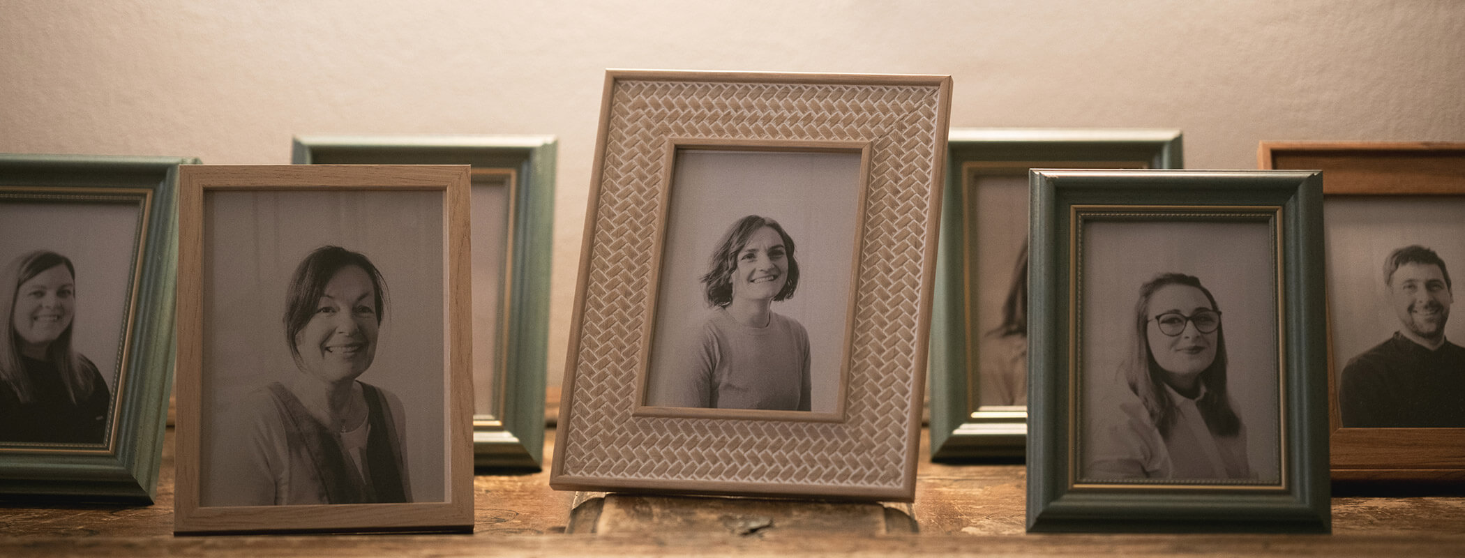 Sechs gerahmte Schwarz-Weiß-Porträts auf einer hölzernen Oberfläche vor einem hellen Hintergrund. - Hotel La Casies Mountain Living