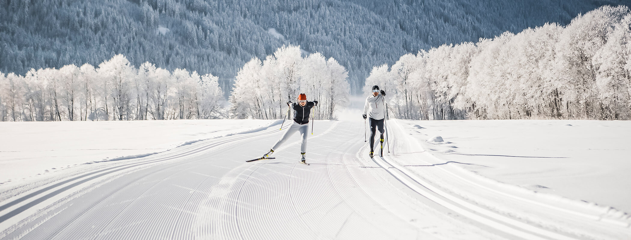 Zwei Personen beim Skilanglauf auf präparierten, verschneiten Loipen mit vereisten Bäumen und Bergen im Hintergrund. - Hotel La Casies Mountain Living