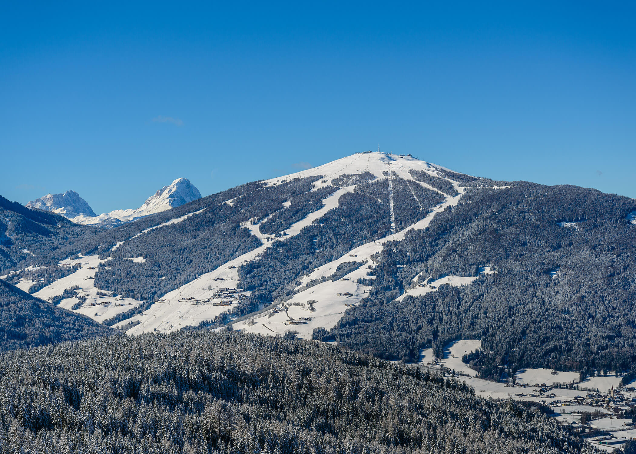 Schneebedeckter Berg mit Skipisten unter blauem Himmel, umgeben von bewaldeten Hügeln. - Hotel La Casies Mountain Living