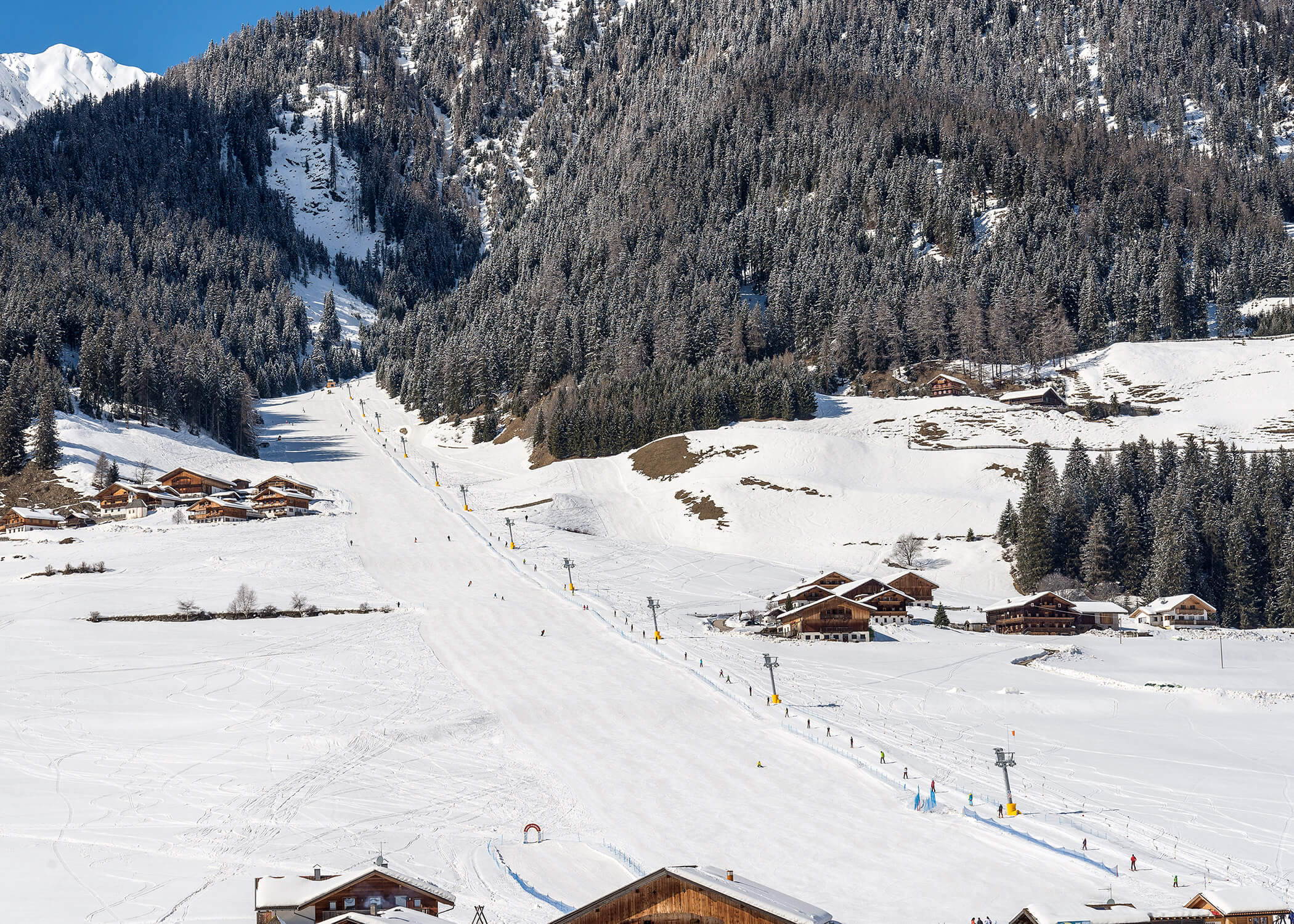 Verschneite Skipiste mit verstreuten Chalets, umgeben von kiefernbedeckten Bergen unter klarem Himmel. - Hotel La Casies Mountain Living