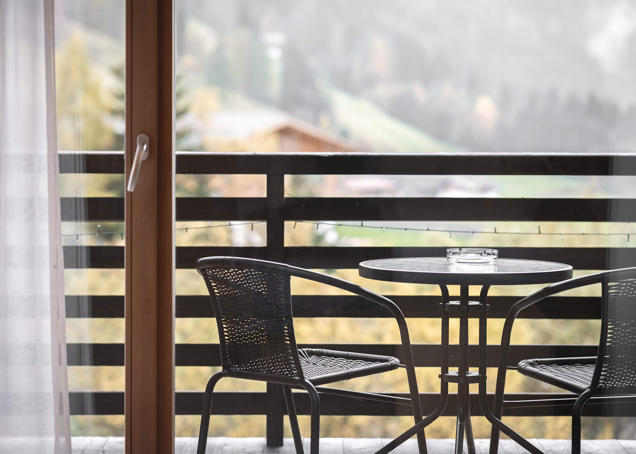Runder Tisch mit zwei schwarzen Stühlen auf einem Balkon mit Blick auf eine verschwommene, neblige Naturlandschaft. - Hotel La Casies Mountain Living