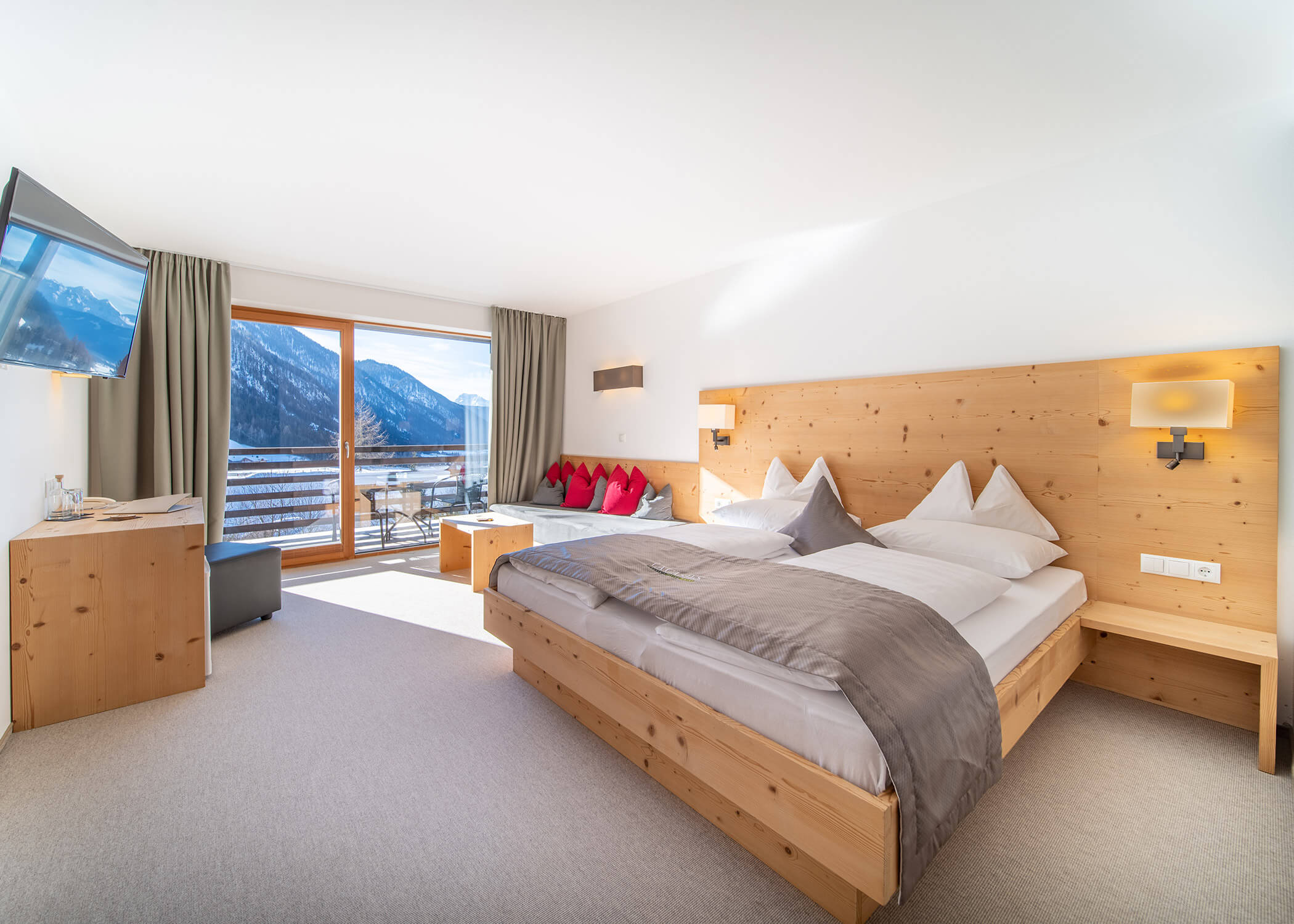 Helles Hotelzimmer mit Holzbett, Sitzecke, TV und Balkon mit Blick auf verschneite Berge. - Hotel La Casies Mountain Living