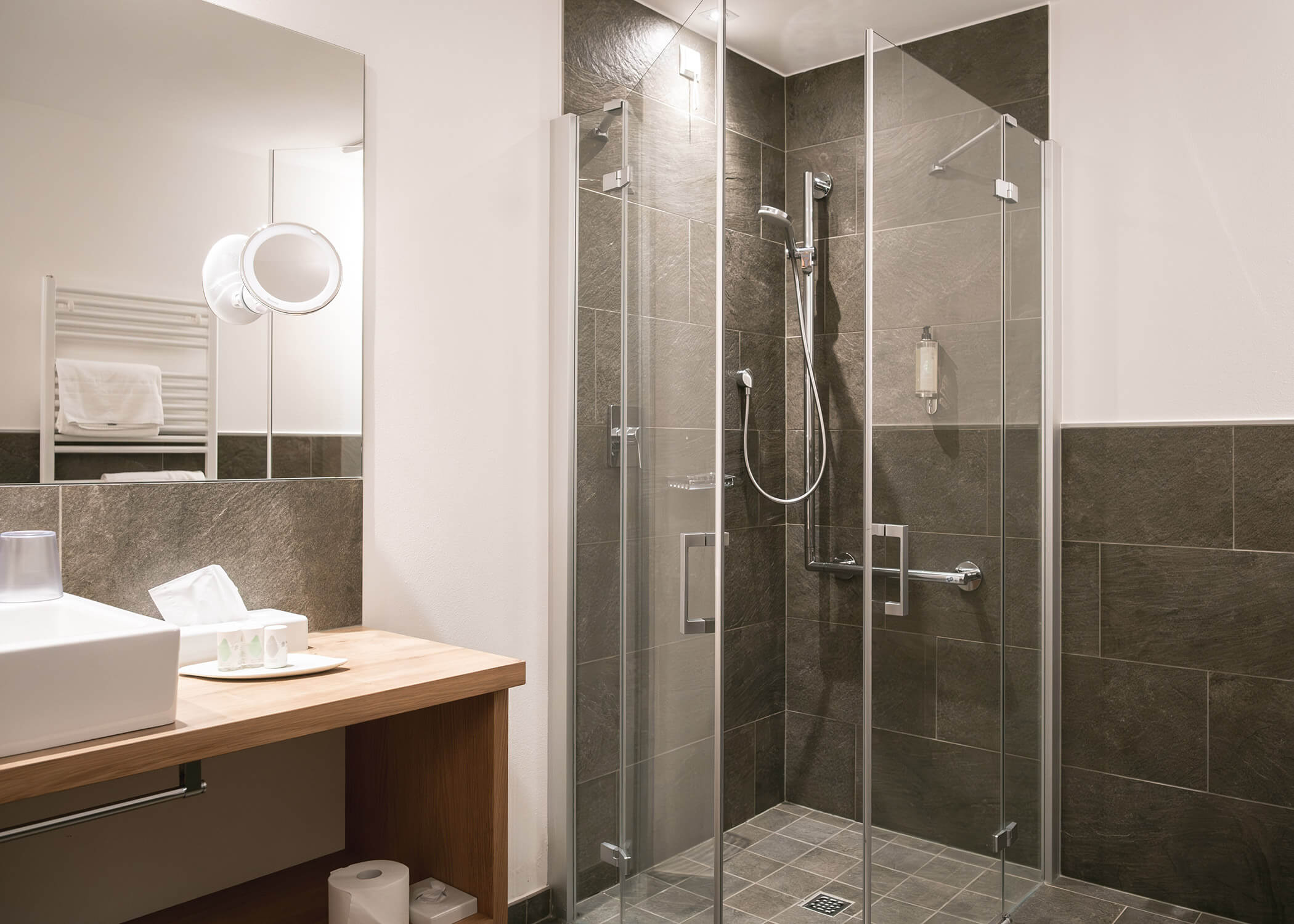 Modernes Badezimmer mit Glasduschabtrennung, Waschbecken, Spiegel und Holzarbeitsplatte. - Hotel La Casies Mountain Living