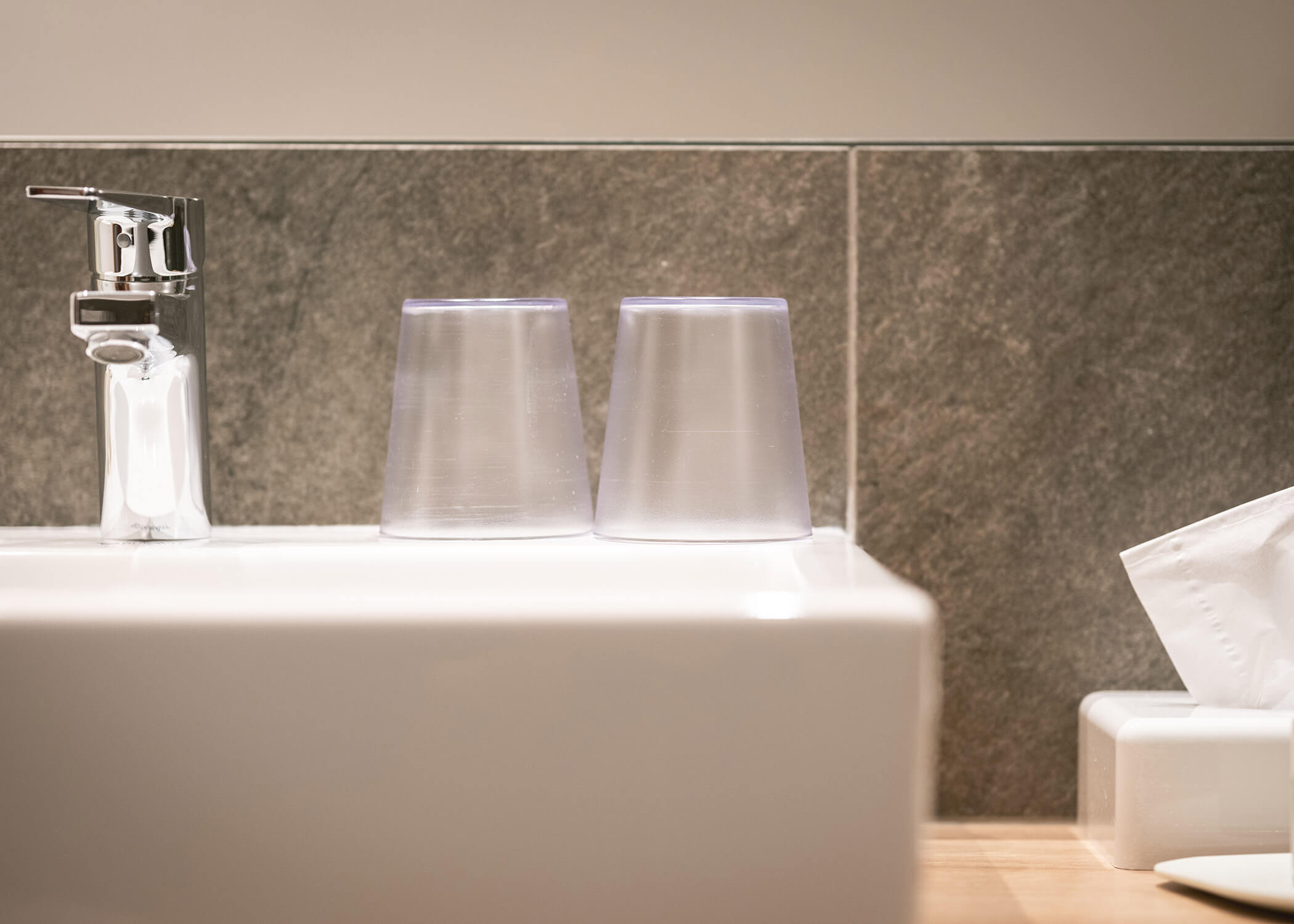 Zwei umgedrehte Plastikbecher auf einem Waschbecken neben einem Wasserhahn und einer Schachtel mit Taschentüchern. - Hotel La Casies Mountain Living