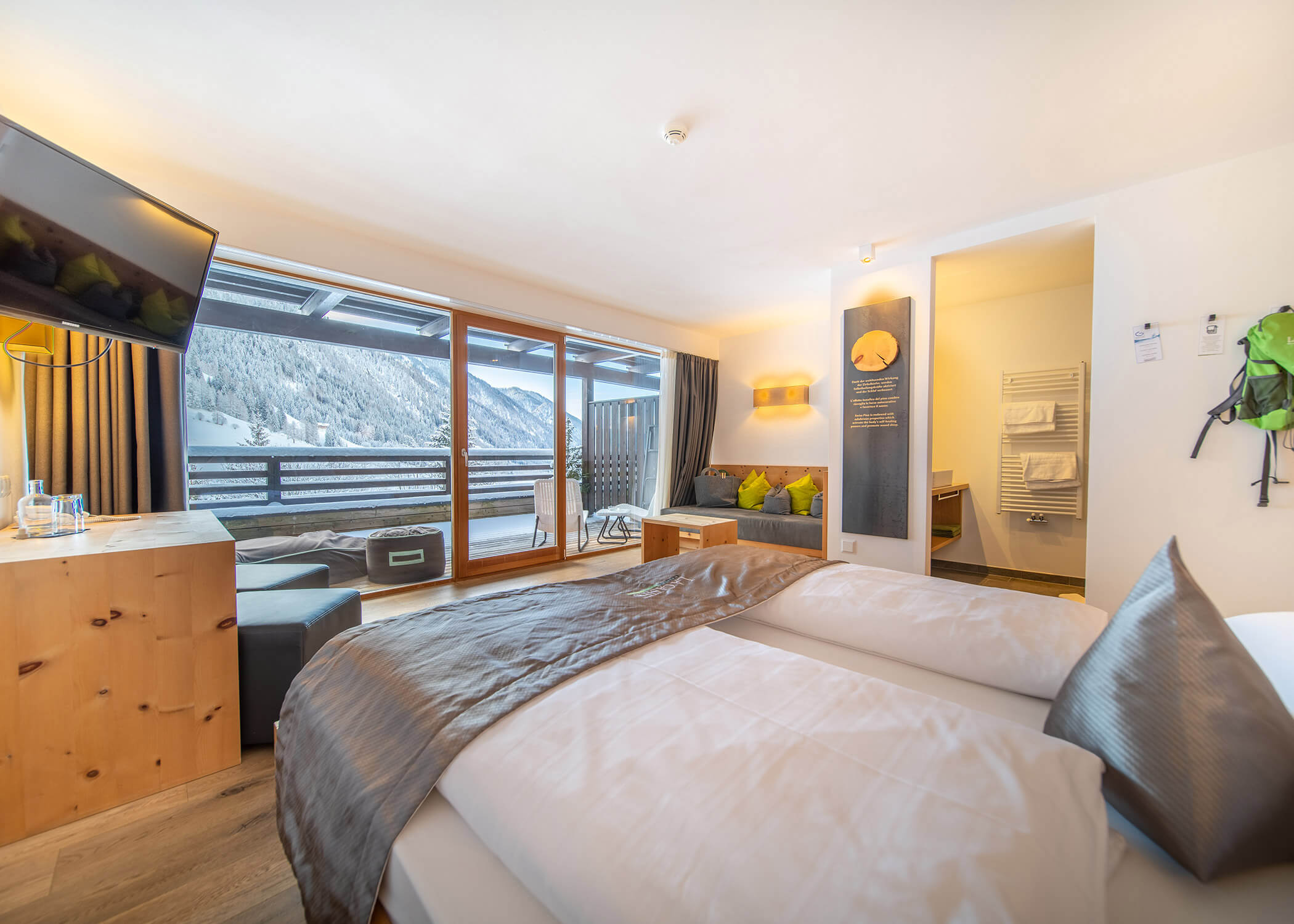 Helles Hotelzimmer mit großem Bett, Balkon, Sofa und Blick auf die verschneiten Berge durch Glastüren. - Hotel La Casies Mountain Living