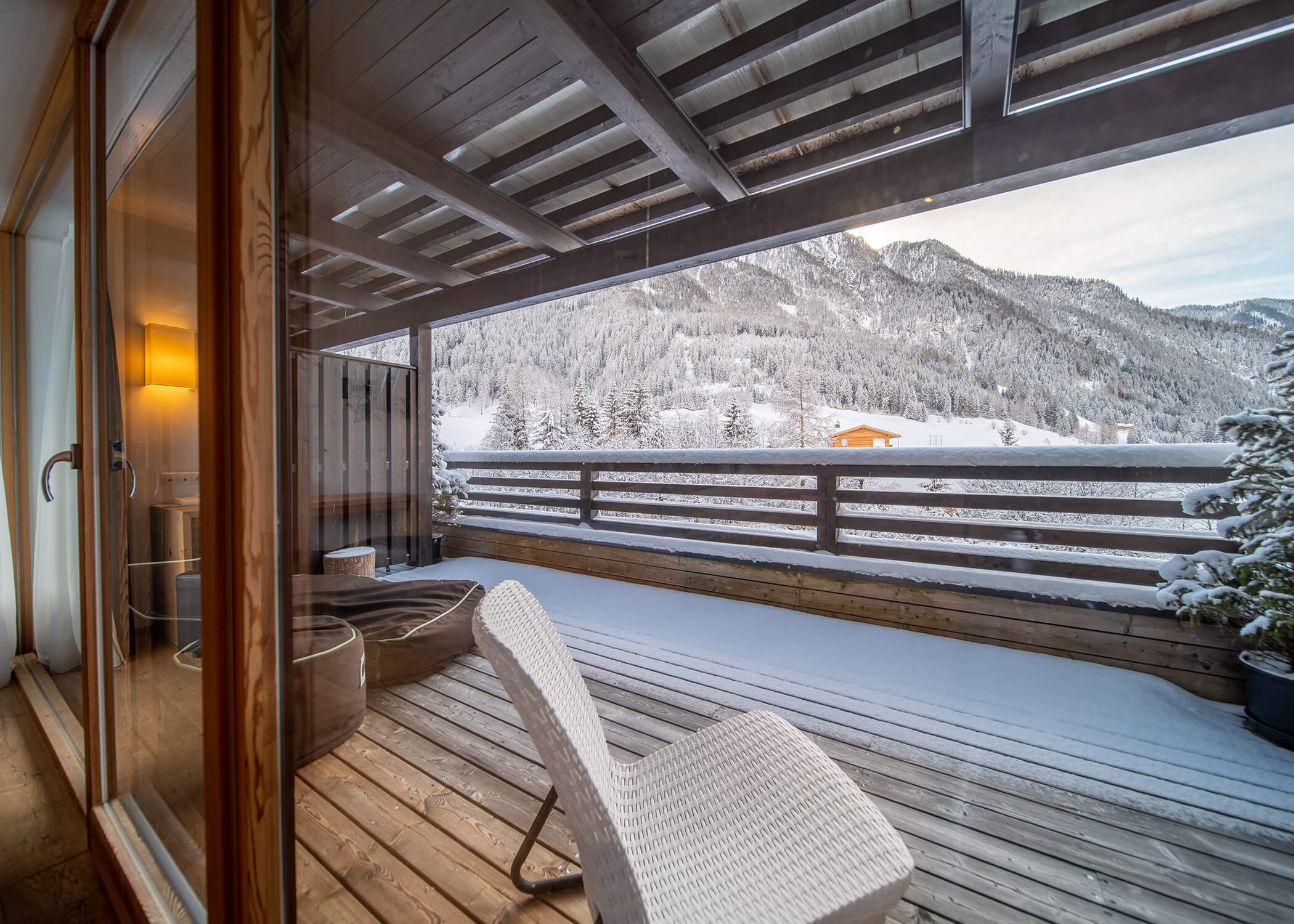 Ein verschneiter Bergblick von einem Holzbalkon mit weißem Stuhl und Geländer unter einem überdachten Dach. - Hotel La Casies Mountain Living