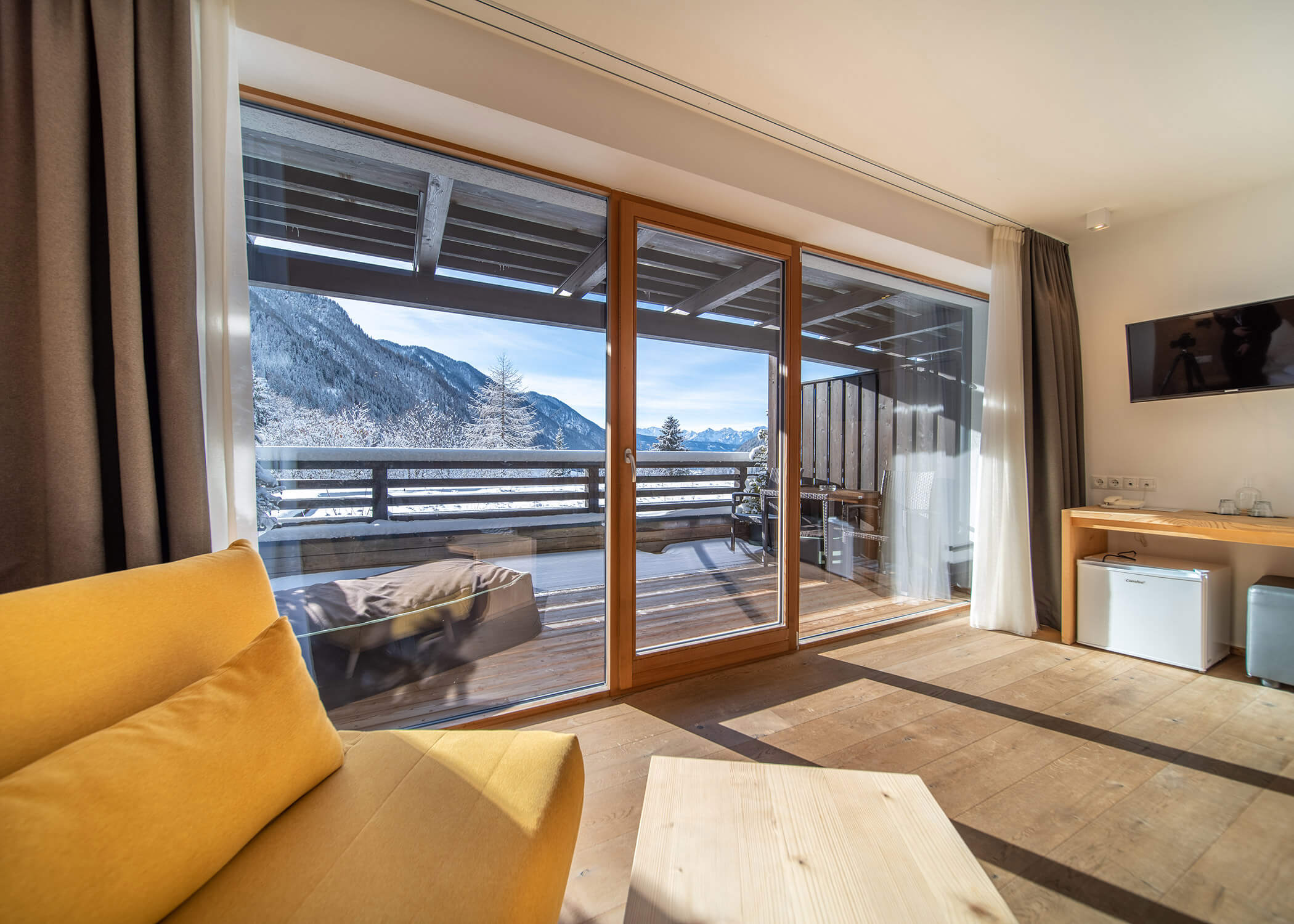 Blick auf die Berge von einem modernen Wohnzimmer mit Holzböden, großen Fenstern und einem gemütlichen Balkon mit Sitzgelegenheiten. - Hotel La Casies Mountain Living
