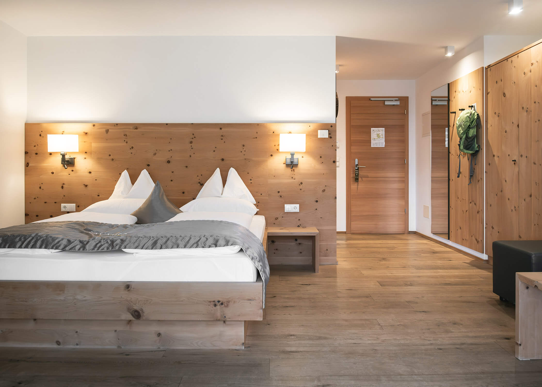 Modernes Hotelzimmer mit zwei Einzelbetten, Holzmöbeln und einem grünen Rucksack, der an einer Schranktür hängt. - Hotel La Casies Mountain Living