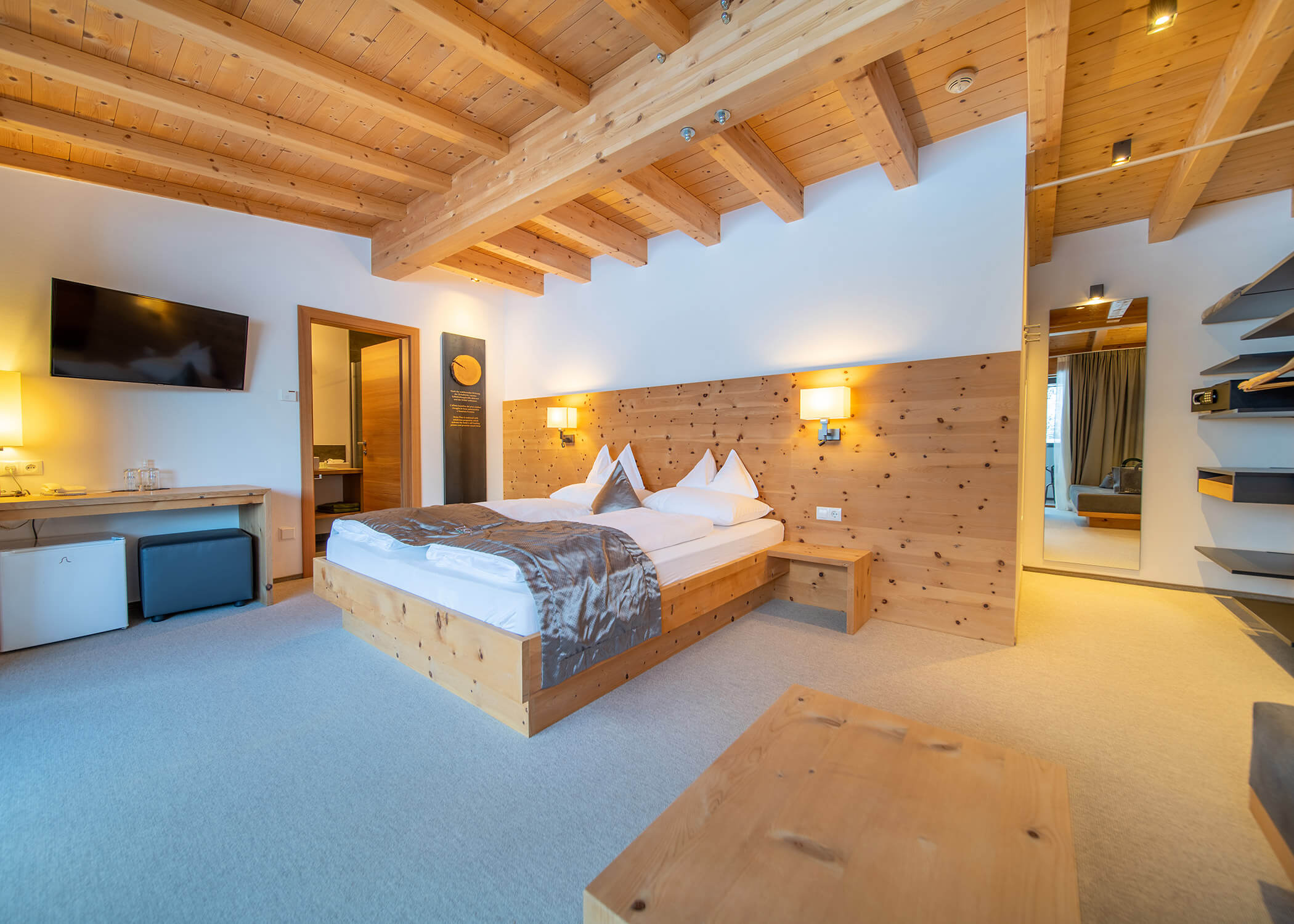 Modernes Hotelzimmer mit Holzbalken, Doppelbett, TV und gemütlicher Beleuchtung in minimalistischem Design. - Hotel La Casies Mountain Living