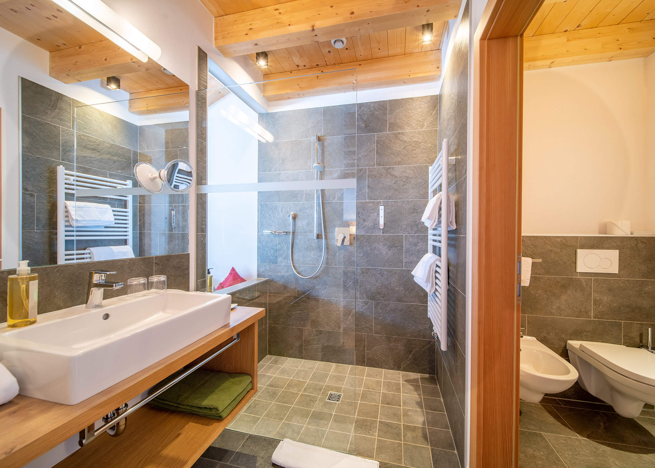 Modernes Badezimmer mit begehbarer Dusche, Waschbecken, Bidet, Handtüchern und Holzdeckenakzenten. - Hotel La Casies Mountain Living