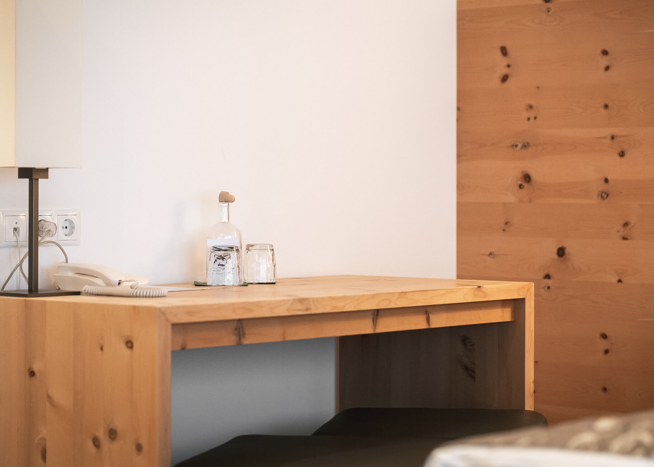 Ein Holztisch mit einem Telefon, einer Glasflasche und zwei Gläsern vor einer weißen Holzwand. - Hotel La Casies Mountain Living
