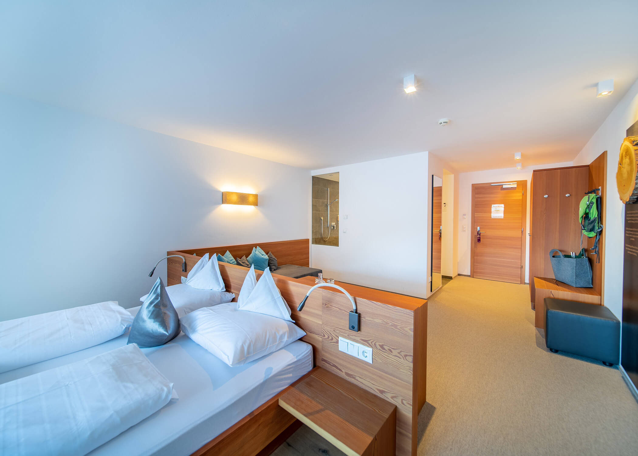 Hotelzimmer mit zwei Betten, einem Sofa, einer Wandleuchte und einem Blick auf die Tür und den Eingangsbereich im Hintergrund. - Hotel La Casies Mountain Living