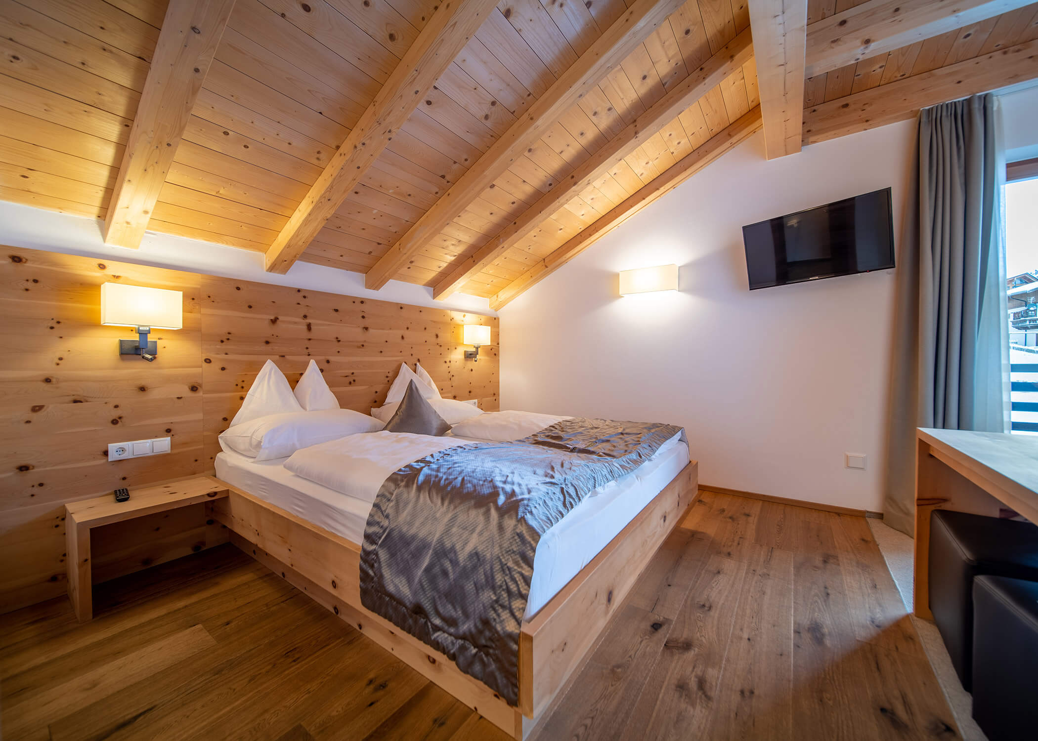 Gemütliches Schlafzimmer im Dachgeschoss mit Holzdecke, Doppelbett, TV an der Wand und natürlichem Licht durch ein Fenster. - Hotel La Casies Mountain Living