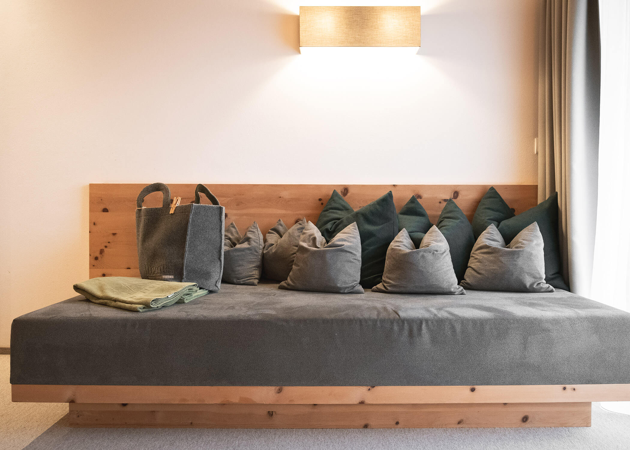 Ein modernes Tagesbett aus Holz mit grauen Kissen, grünen Wurfkissen, einem gefalteten Handtuch und einer Tragetasche. - Hotel La Casies Mountain Living