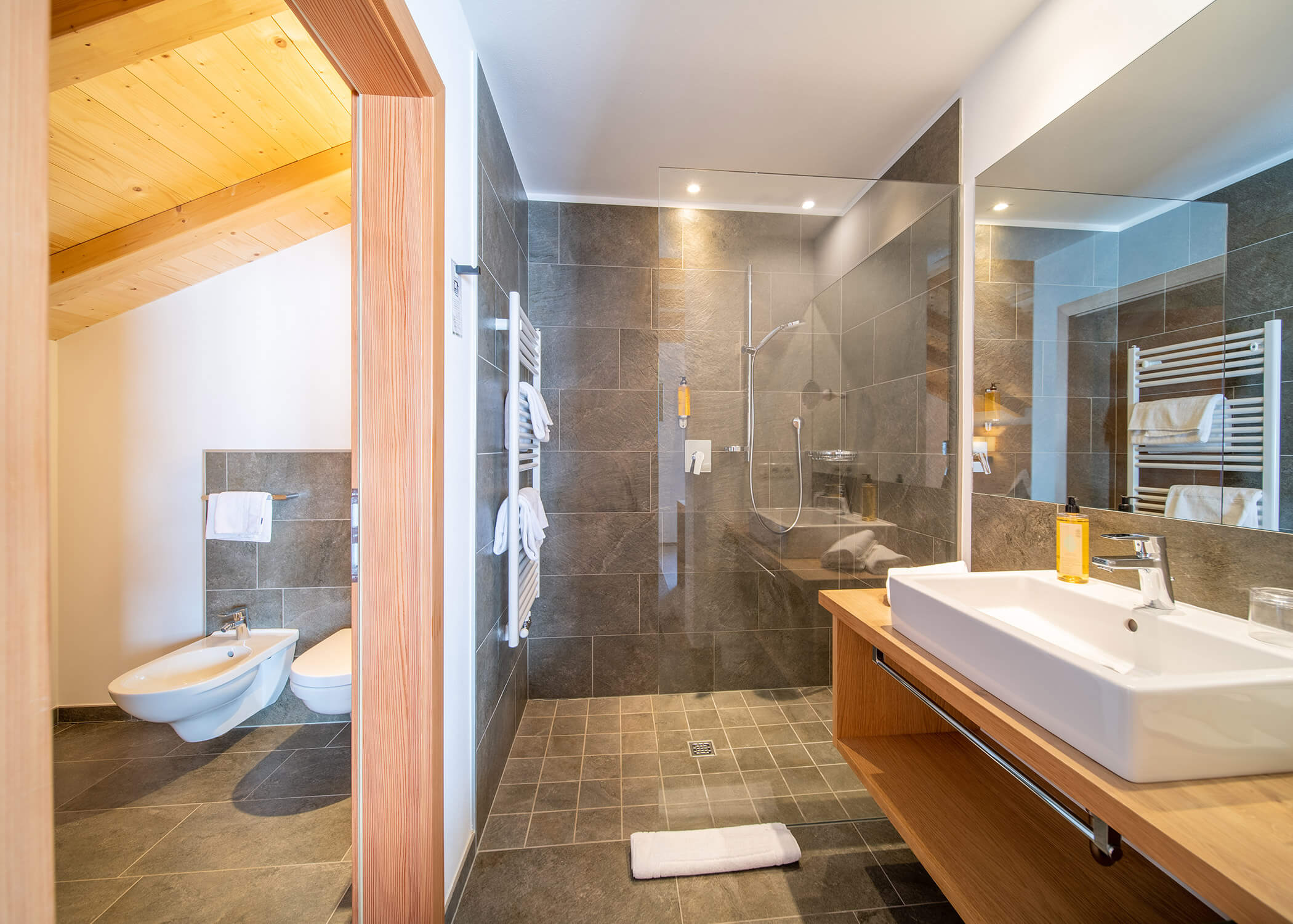 Modernes Badezimmer mit begehbarer Dusche, Waschbecken, Spiegel, Bidet, Toilette und Holzakzenten. - Hotel La Casies Mountain Living