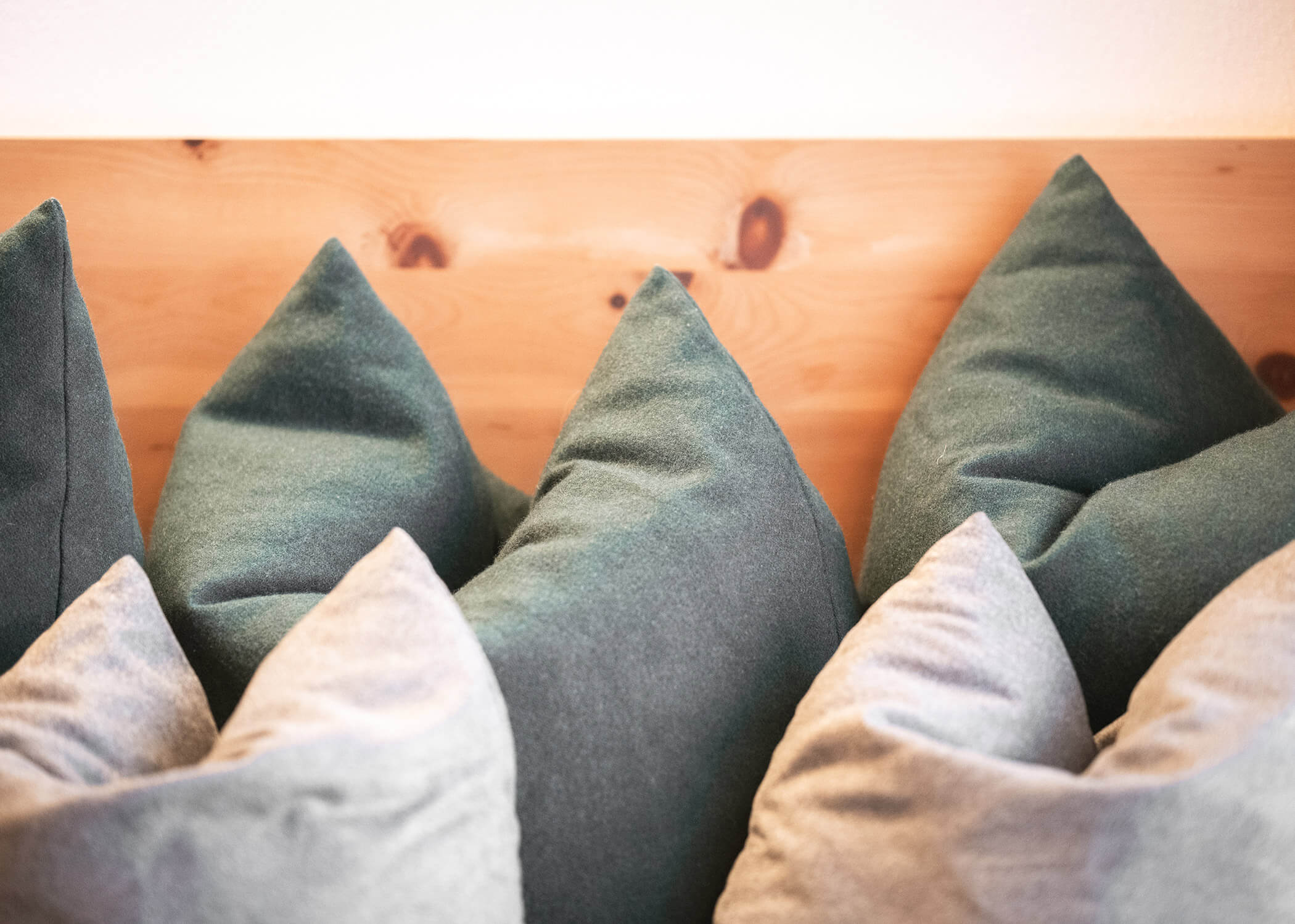 Sechs Plüschkissen mit grünen und beigen Bezügen sind vor einem hölzernen Kopfteil angeordnet. - Hotel La Casies Mountain Living