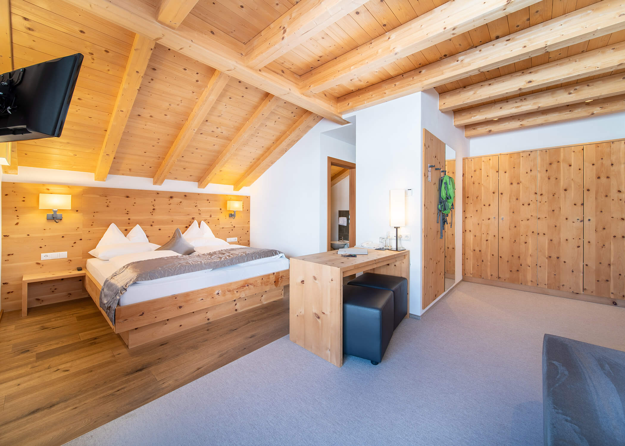 Gemütliches Schlafzimmer mit Holzdecke und -wänden, einem Doppelbett, Schreibtisch, Fernseher und gedämpfter Beleuchtung. - Hotel La Casies Mountain Living