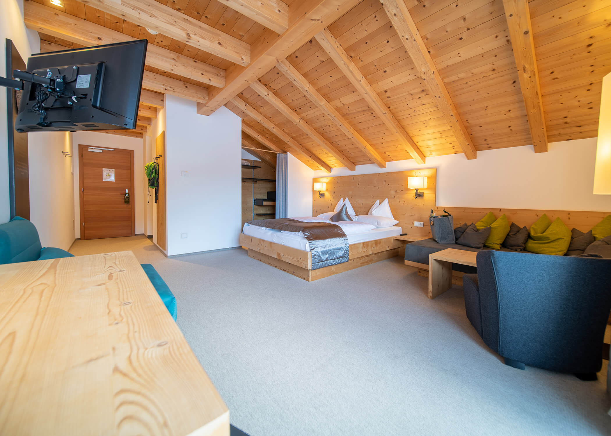 Gemütliches Hotelzimmer mit Holzbalkendecke, Doppelbett, Sofa, TV, Schreibtisch und warmer Beleuchtung. - Hotel La Casies Mountain Living