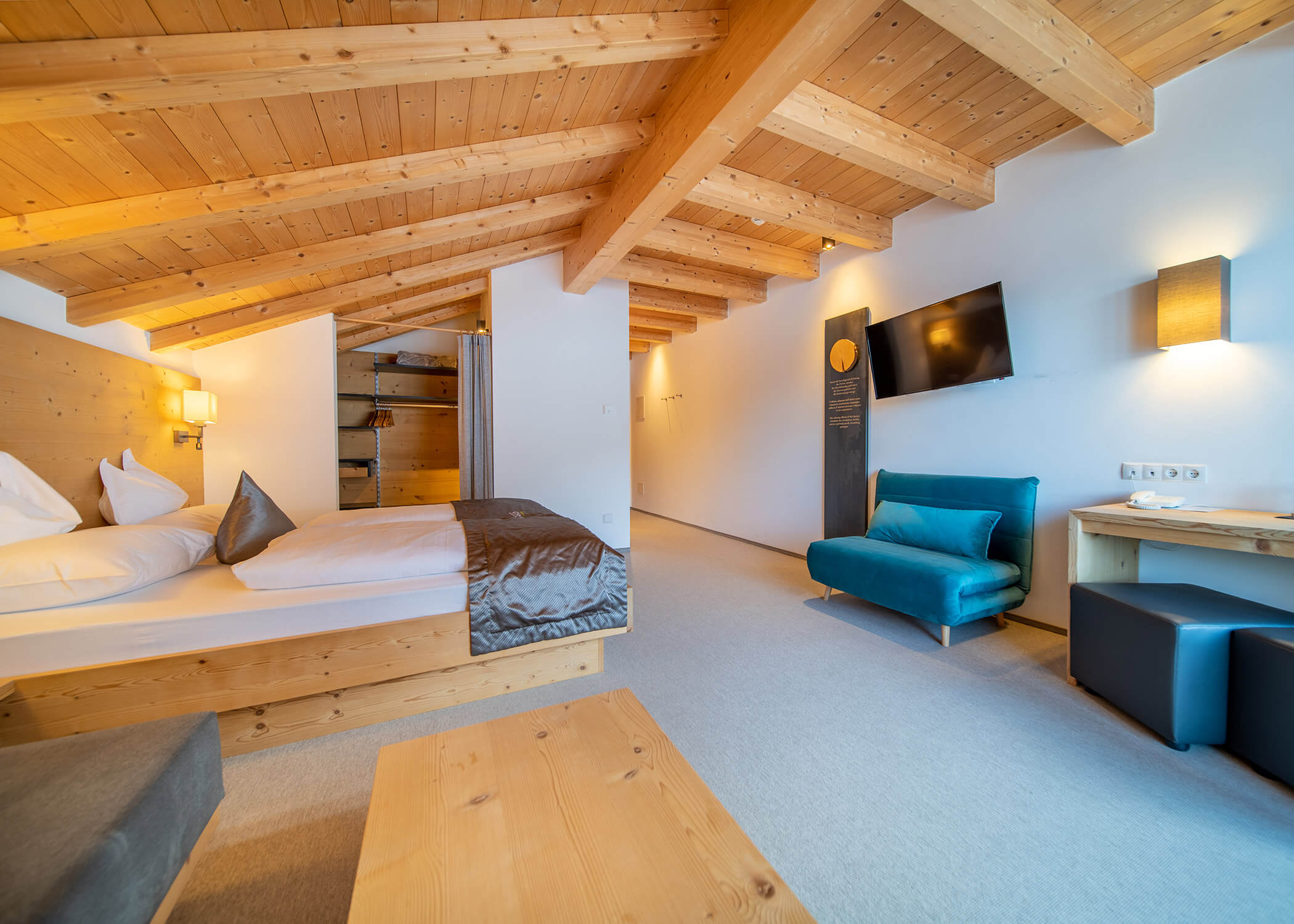 Gemütliches Hotelzimmer mit Holzdecke, Doppelbett, Sofa, TV, Regalen und warmer Beleuchtung. - Hotel La Casies Mountain Living