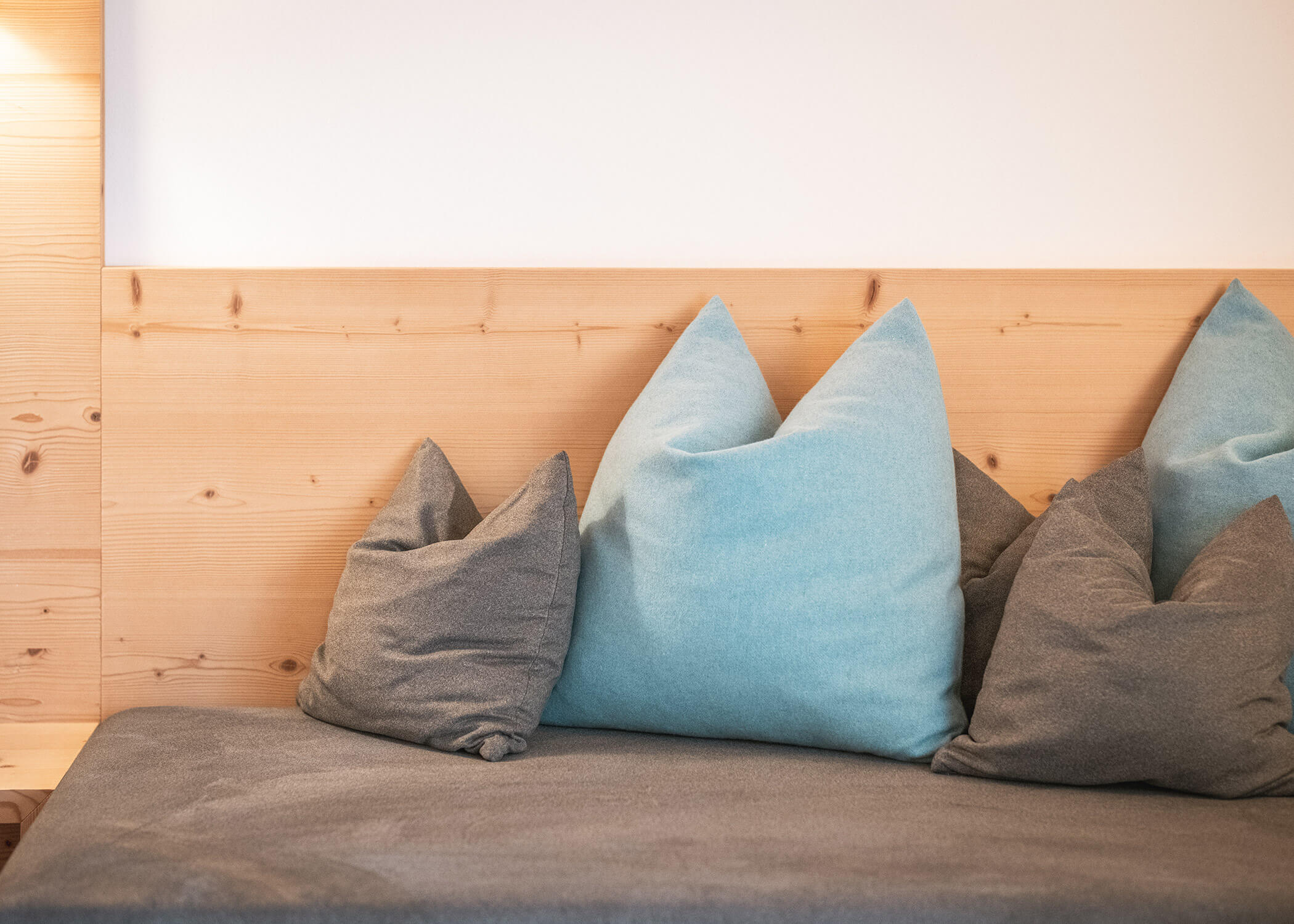 Ein hölzernes Kopfteil mit grauen und hellblauen Kissen auf einem grauen Bettüberwurf. - Hotel La Casies Mountain Living