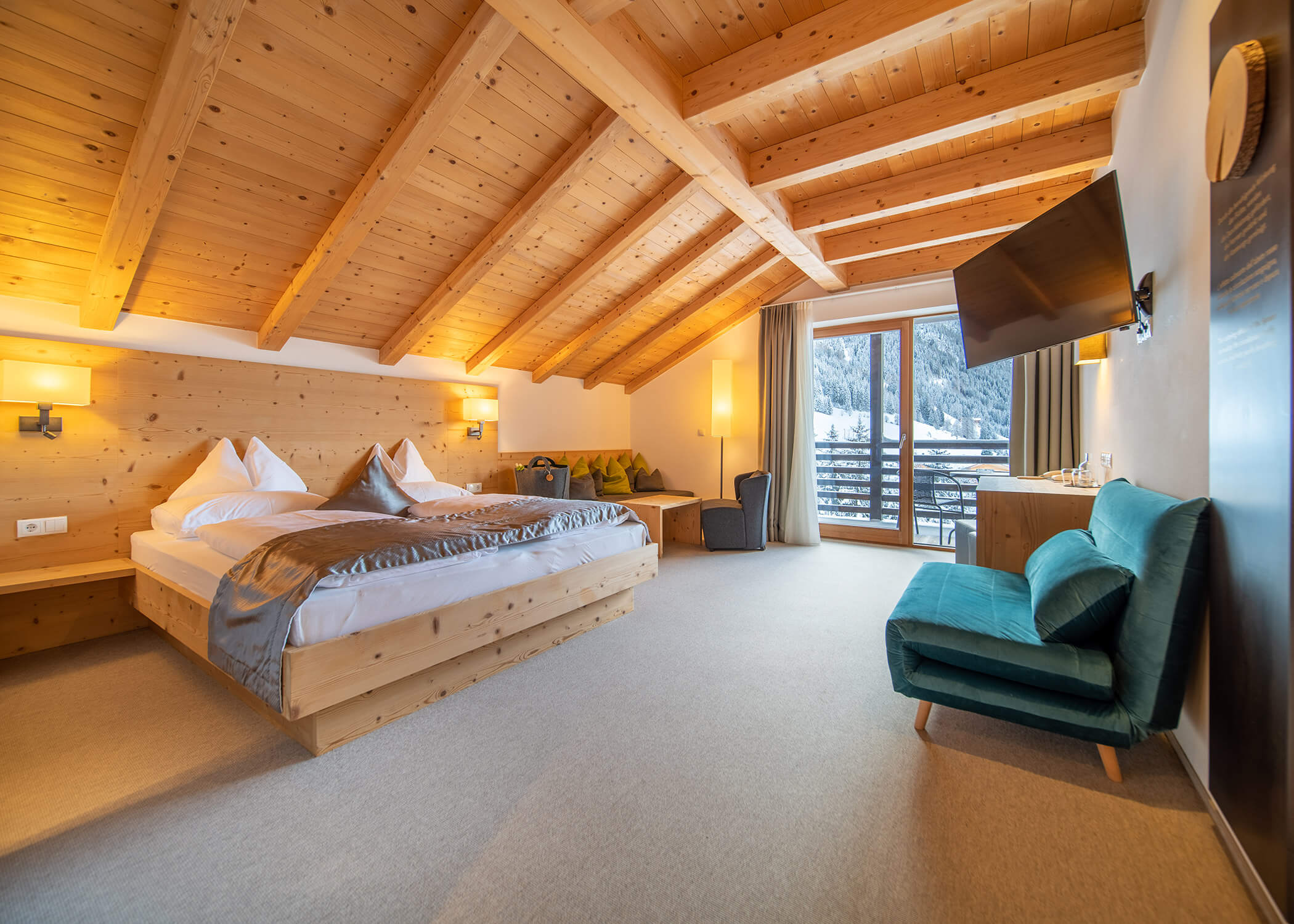 Helles, gemütliches Hotelzimmer mit Holzdecke, Doppelbett, Sofa, Schreibtisch und Balkon mit Blick auf verschneite Berge. - Hotel La Casies Mountain Living