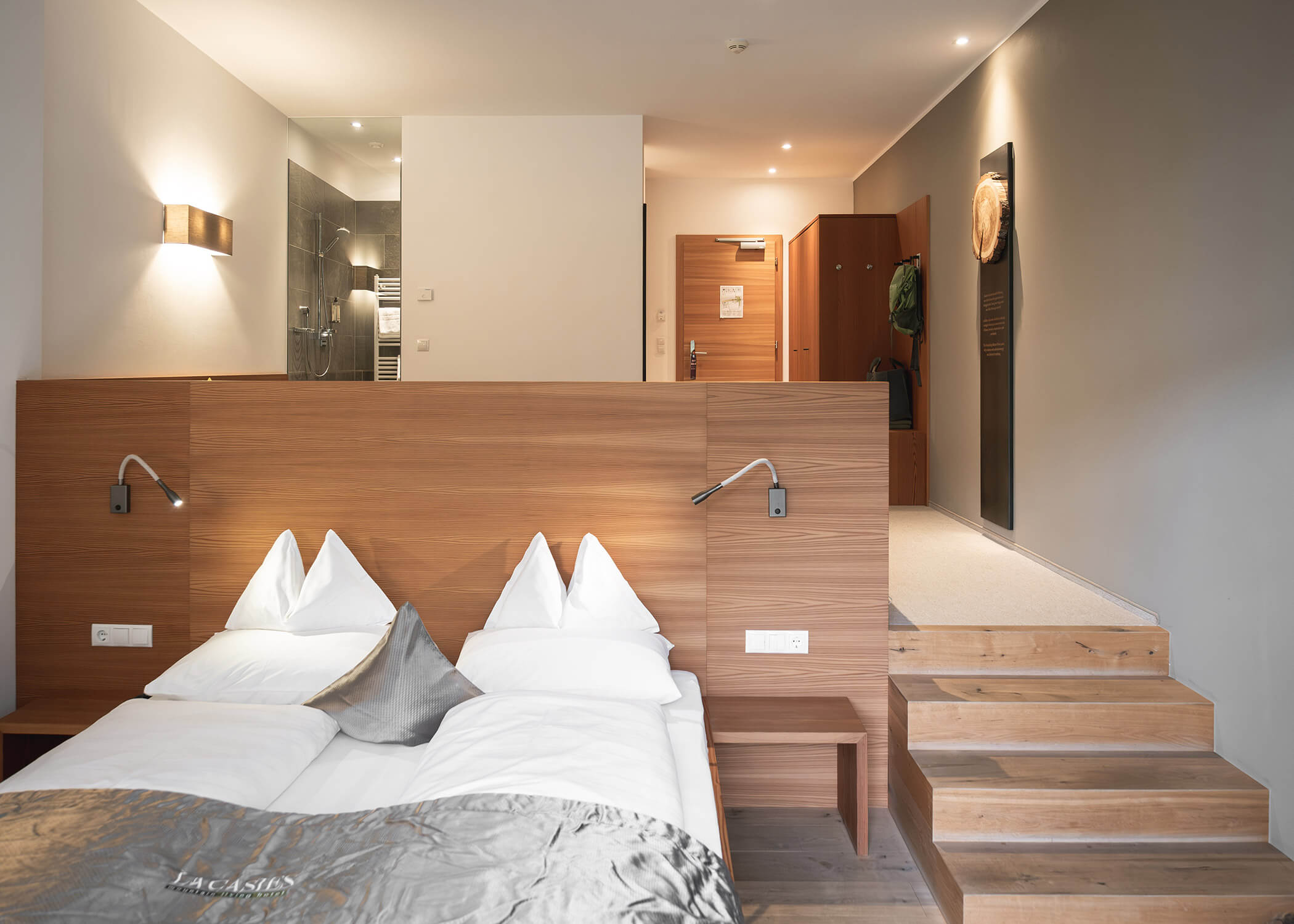 Modernes Hotelzimmer mit einem sauber gemachten Bett, Holzdekor und einem erhöhten Bereich, der zum Eingang und zum Bad führt. - Hotel La Casies Mountain Living