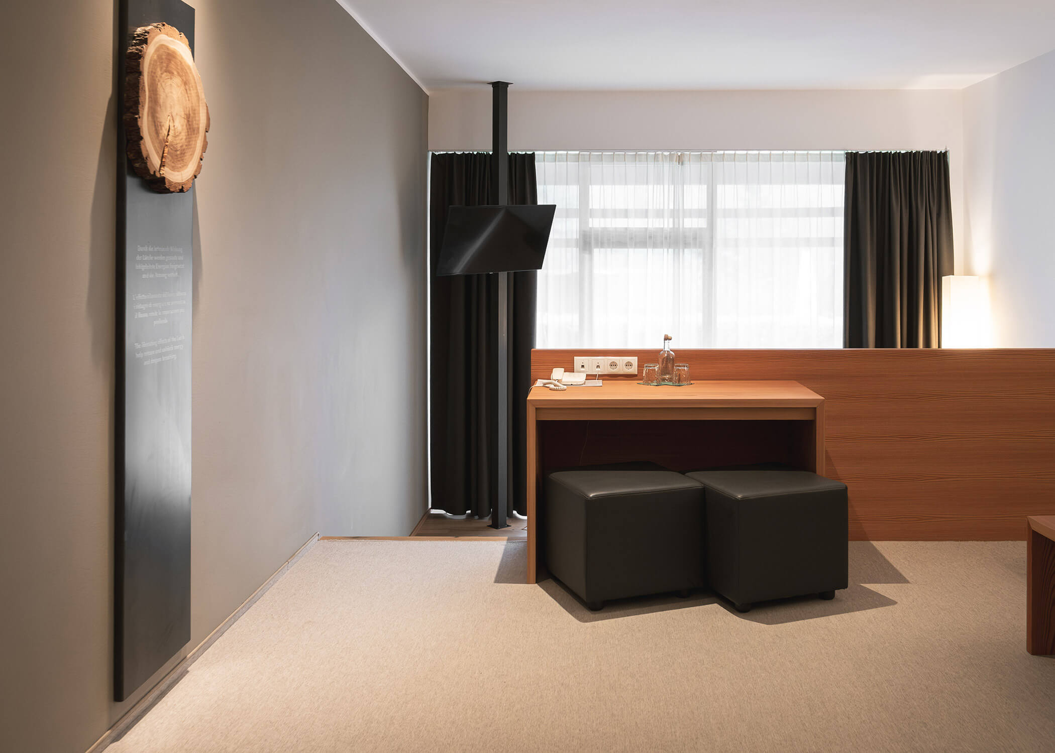 Minimalistisches Hotelzimmer mit Holzschreibtisch, zwei schwarzen Hockern, großem Fenster und moderner Einrichtung. - Hotel La Casies Mountain Living