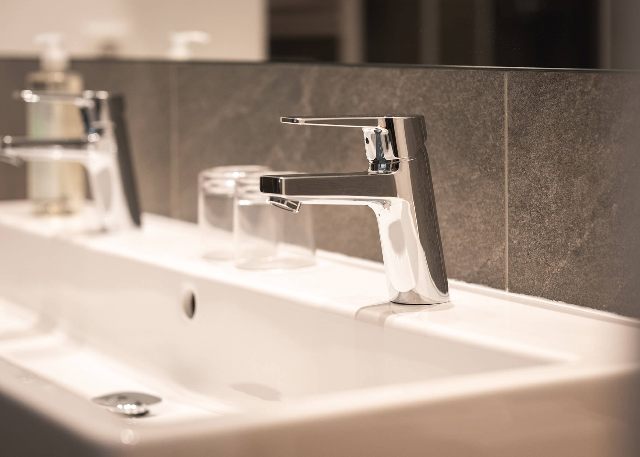 Nahaufnahme einer modernen verchromten Badezimmerarmatur mit Glas und Seifenspender auf einem weißen Waschbecken. - Hotel La Casies Mountain Living