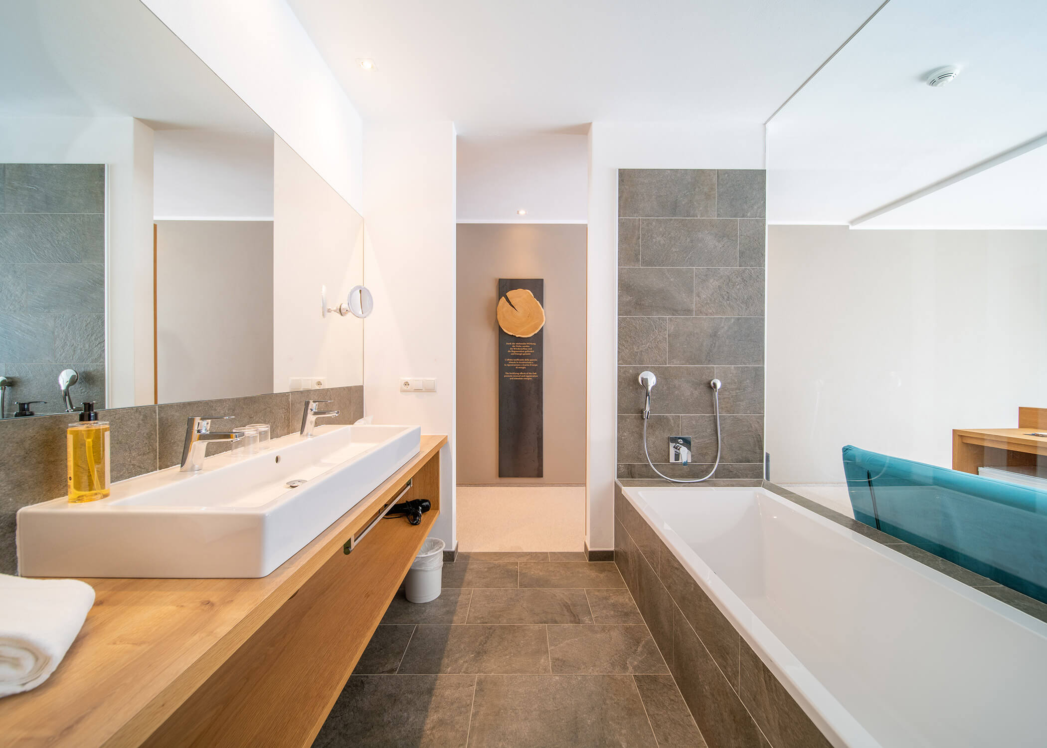Modernes Badezimmer mit Doppelwaschbecken, großem Spiegel, Badewanne und neutralen Fliesen und Holzakzenten. - Hotel La Casies Mountain Living