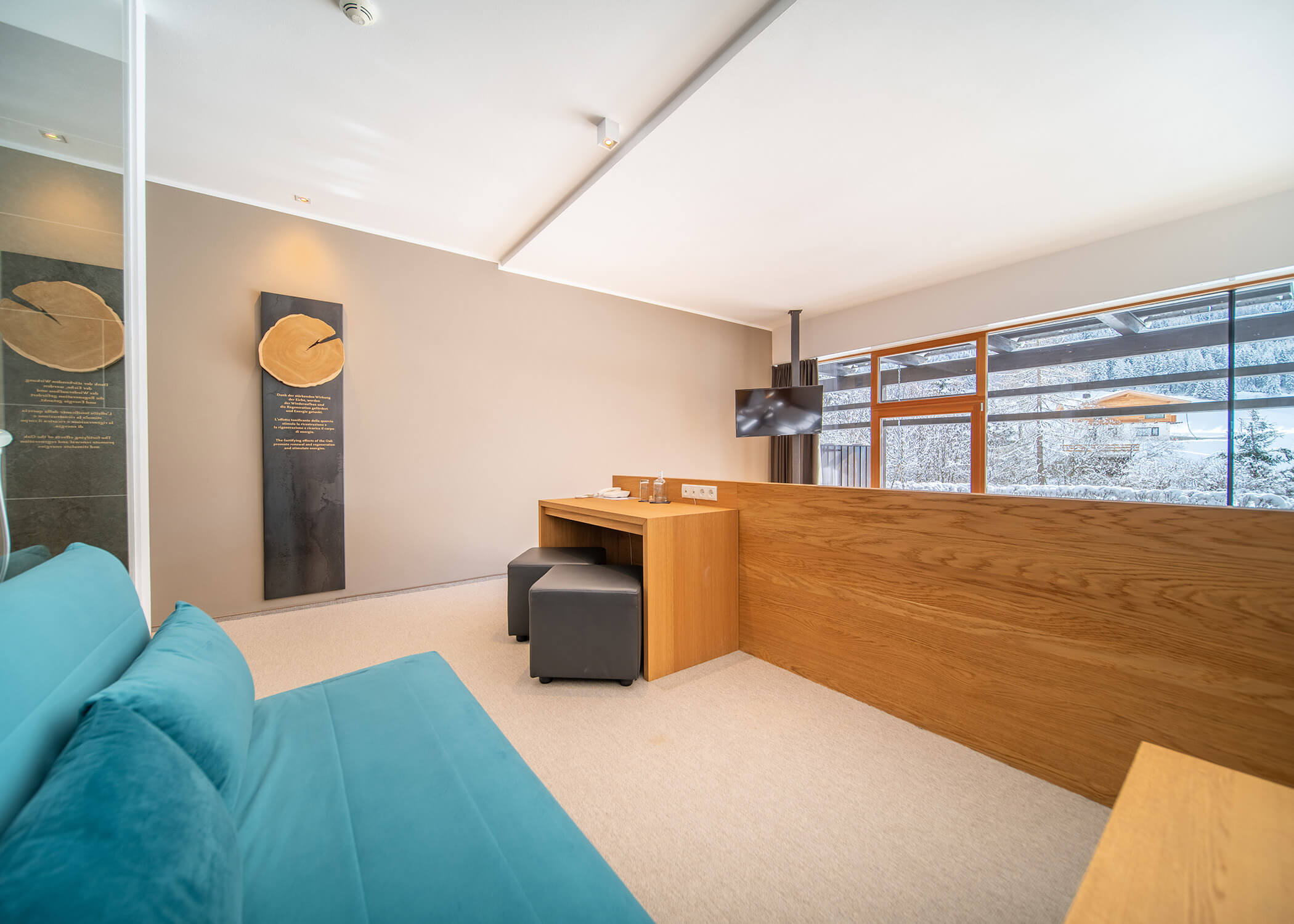 Moderner Empfangsbereich mit einem Holzschreibtisch, einem blauen Sofa, großen Fenstern und zwei schwarzen Hockern. - Hotel La Casies Mountain Living
