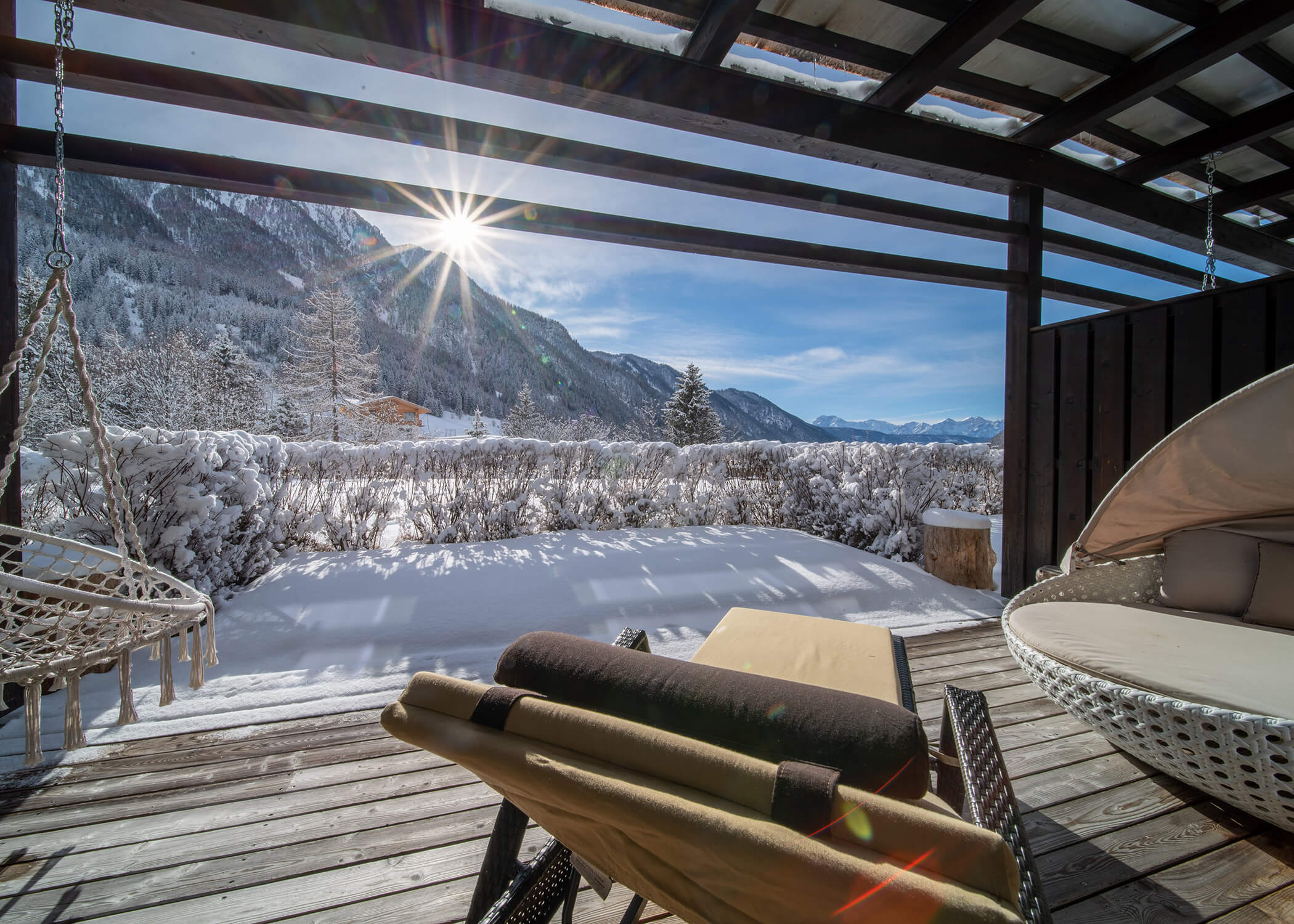 Ein verschneiter Bergblick von einer gemütlichen Holzterrasse mit Liegestühlen und Hängeschaukeln unter einer Überdachung. - Hotel La Casies Mountain Living