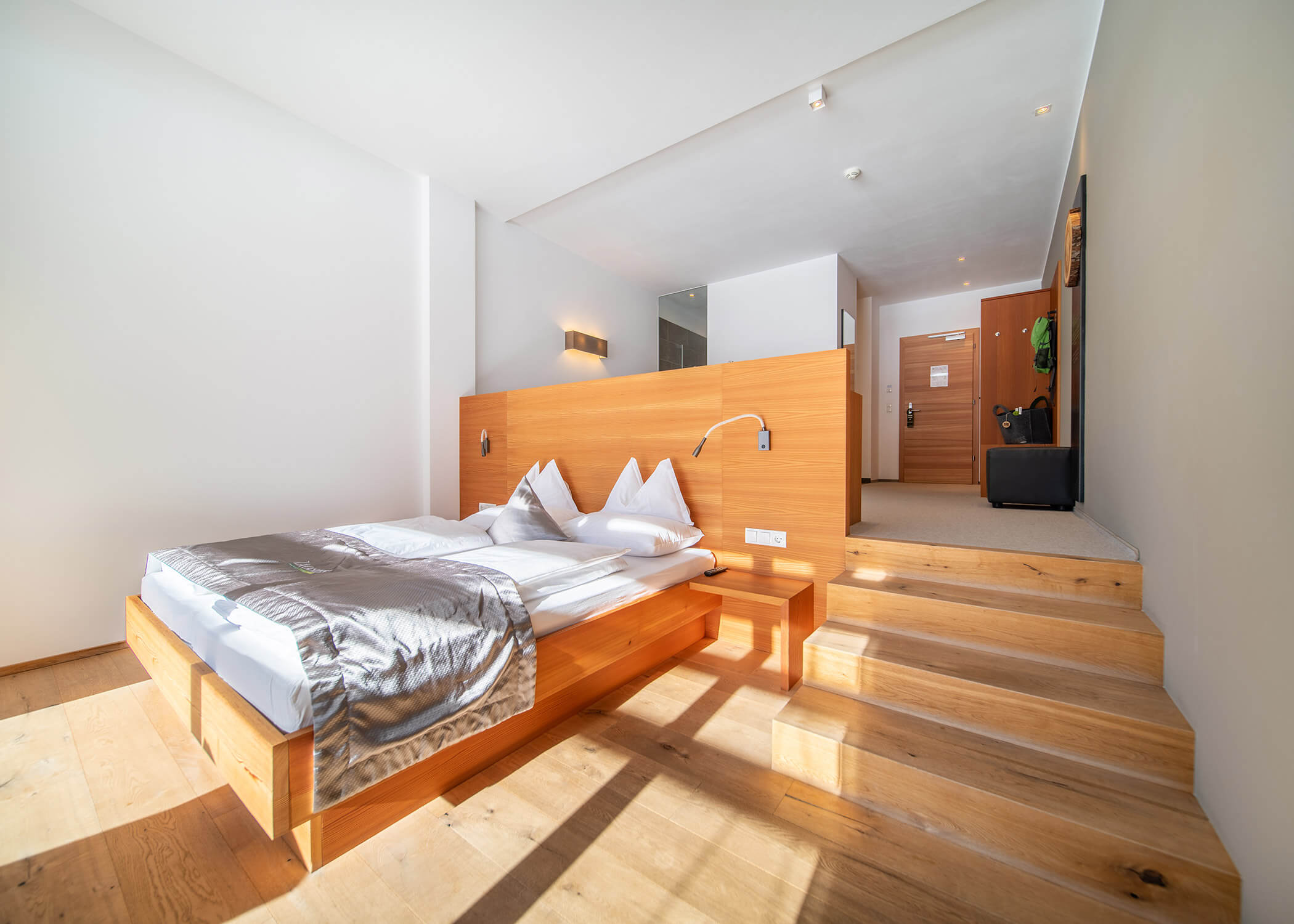 Modernes Hotelzimmer mit Holzboden, Podestbett, Treppe und minimalistischem Dekor in natürlichem Licht. - Hotel La Casies Mountain Living