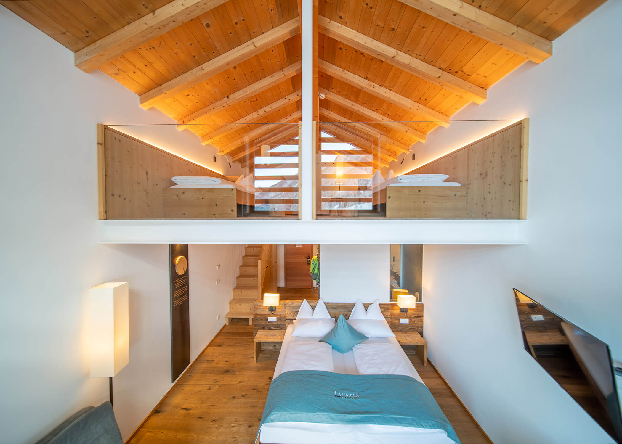 Modernes Loft-Schlafzimmer mit Holzdecke, Glastrennwand, Doppelbetten und warmer Raumbeleuchtung. - Hotel La Casies Mountain Living