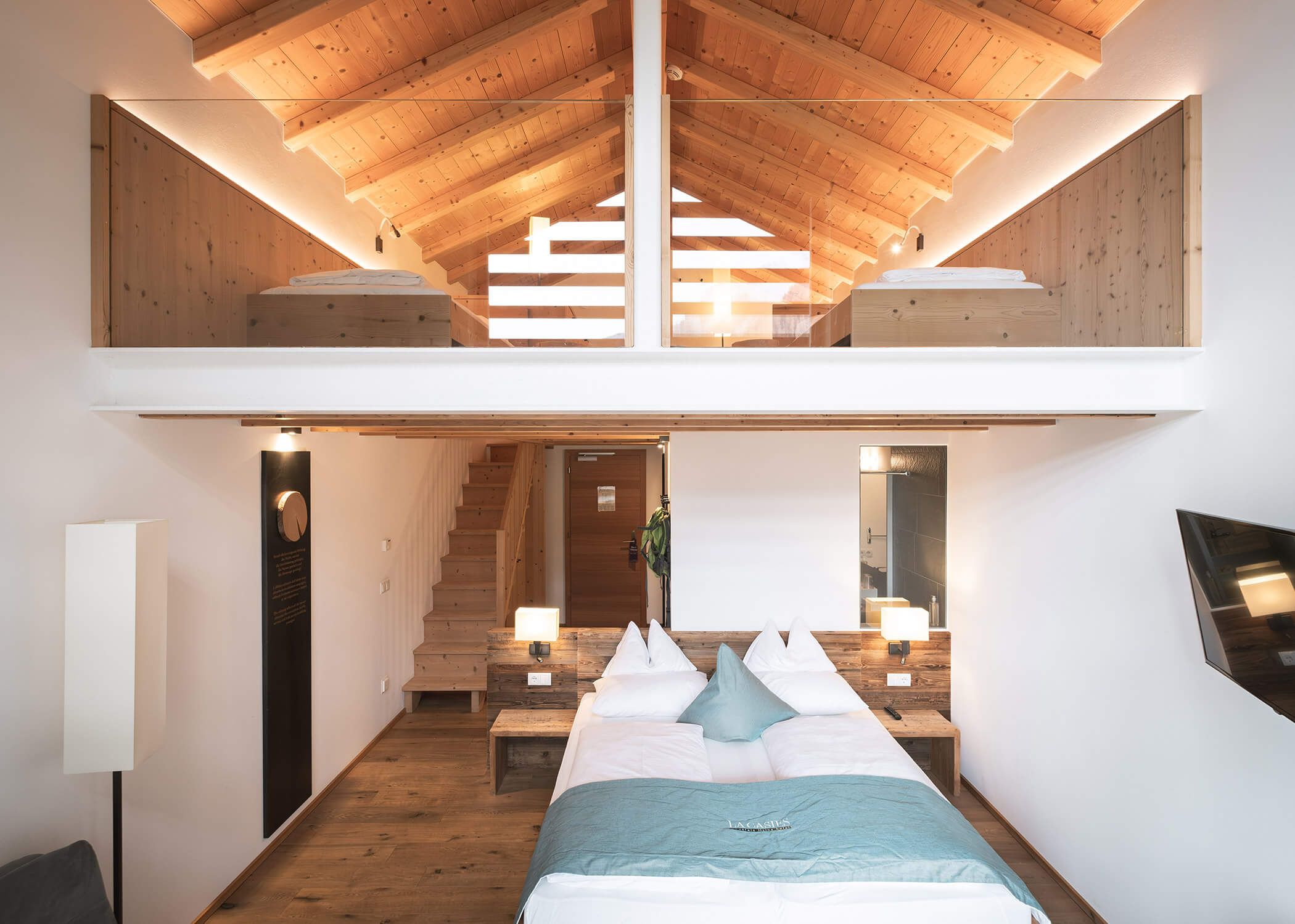 Modernes Loft-Schlafzimmer mit Holzdecke, Doppelbett, Glasgeländer und einer Treppe zum oberen Stockwerk. - Hotel La Casies Mountain Living